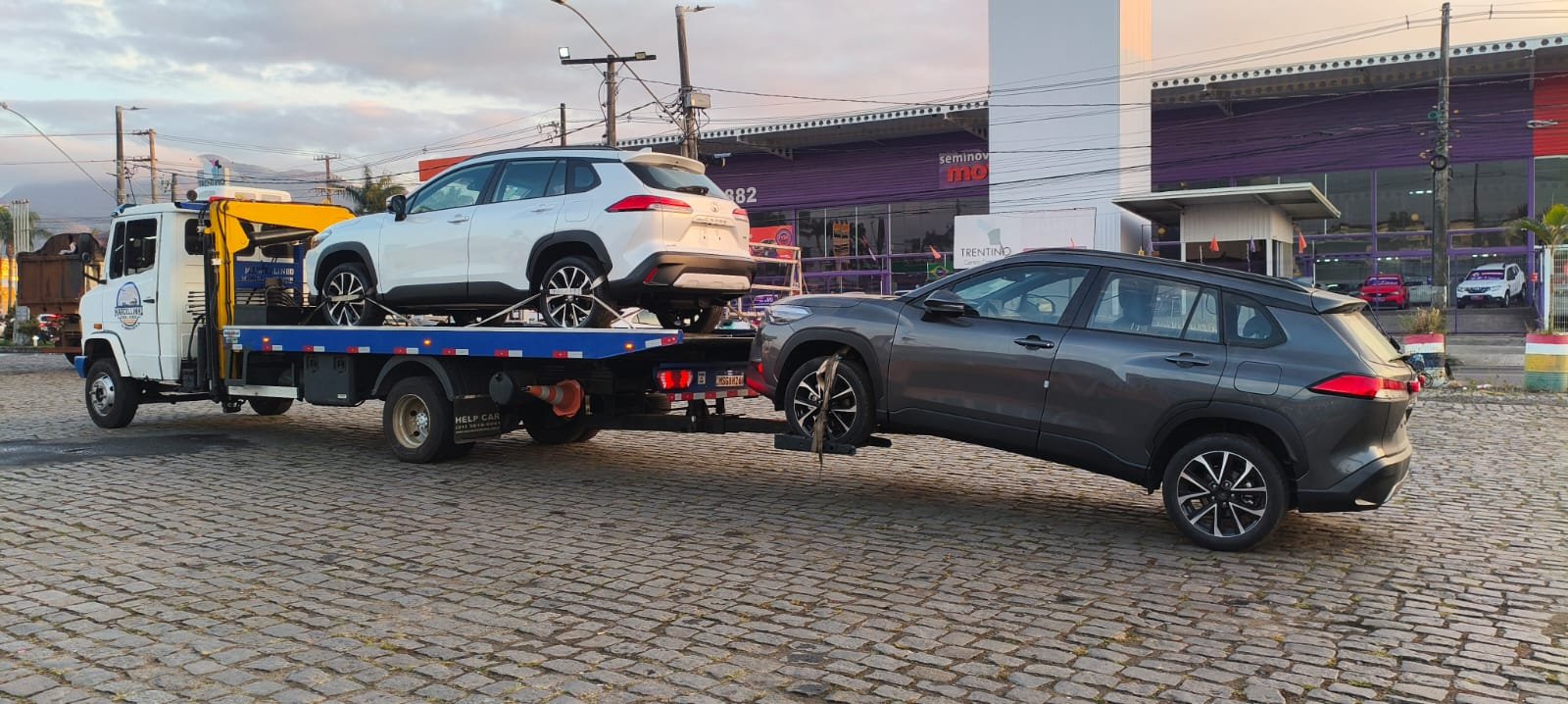 Dois SUVs Corolla Cross: um branco na plataforma e um cinza engatado atrás.
